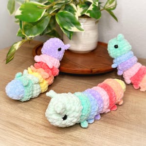 May include: Three rainbow-colored crocheted caterpillar toys. The caterpillars are made of soft, fluffy yarn and have a pastel color scheme.