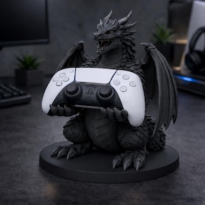 May include: A black and gray dragon statue holding a white and black game controller. The dragon has detailed scales, wings, and horns. The controller has a sleek design with multiple buttons and a central touchpad. The statue sits on a round black base.