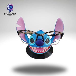 Op de afbeelding: Blauw Stitch-personage met grote tanden die een zwart-witte schildpadbril draagt. Het personage is een brillenhouder.