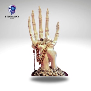 Puede incluir: Una mano esquelética blanca con joyas de oro y plata en los dedos y la muñeca. La mano descansa sobre una base de pequeños cráneos blancos.