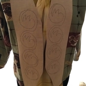 May include: A beige waistcoat with a V-neck and a pattern of stitched circles on the front. The waistcoat is made of a soft, textured fabric and has a relaxed fit.