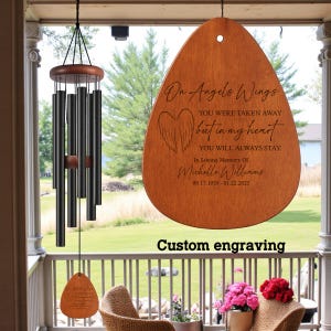 Könnte beinhalten: Ein Holzwindspiel mit schwarzen Röhren und einem tropfenförmigen Holzanhänger. Der Anhänger ist mit dem Text "On Angels Wings" und einer Gedenknachricht graviert. Der Satz "Custom engraving" ist ebenfalls sichtbar.