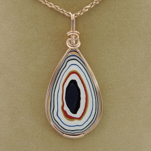 May include: A teardrop-shaped pendant with a colorful agate stone set in a gold wire wrap. The stone has concentric rings of white, blue, green, red, and black.