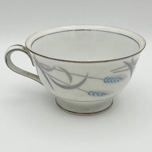 May include: A white teacup with a gold rim and a delicate floral design featuring blue and gray wheat stalks.