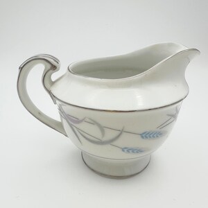 May include: White porcelain creamer with a silver rim and a delicate floral design featuring blue and gray wheat stalks.