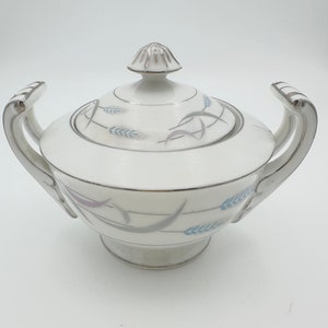 May include: White porcelain sugar bowl with a lid and silver trim. The bowl has a blue and silver wheat design.