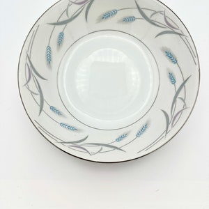 May include: A white ceramic bowl with a silver rim and a blue and gray wheat design.