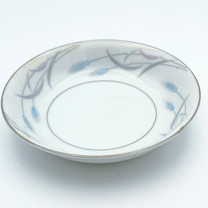 May include: A white porcelain bowl with a silver rim and a delicate floral design in shades of blue and gray. The design features stylized wheat stalks and leaves.