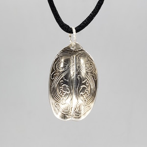May include: A silver pendant necklace with a detailed floral design. The pendant is shaped like a teardrop and hangs from a black cord.