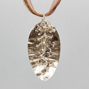 May include: A silver pendant necklace with a teardrop-shaped design. The pendant is filled with clear quartz crystals and has a brown ribbon attached.