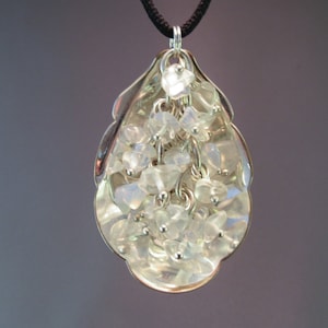 May include: A silver teardrop-shaped pendant with a cluster of clear iridescent stones hanging from it.