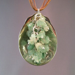 May include: A silver pendant necklace with a green gemstone cluster hanging from a brown leather cord.
