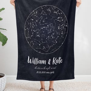 May include: A dark navy blue blanket featuring a white constellation design within a large circle. The blanket has the names "William & Kate" and the text "the stars on the night we met 20.05.2000 new york" in white script.