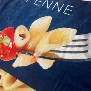 May include: A blue and white box with the word "PENNE" printed on it. The box features a close-up image of cooked penne pasta with a red tomato and a fork.