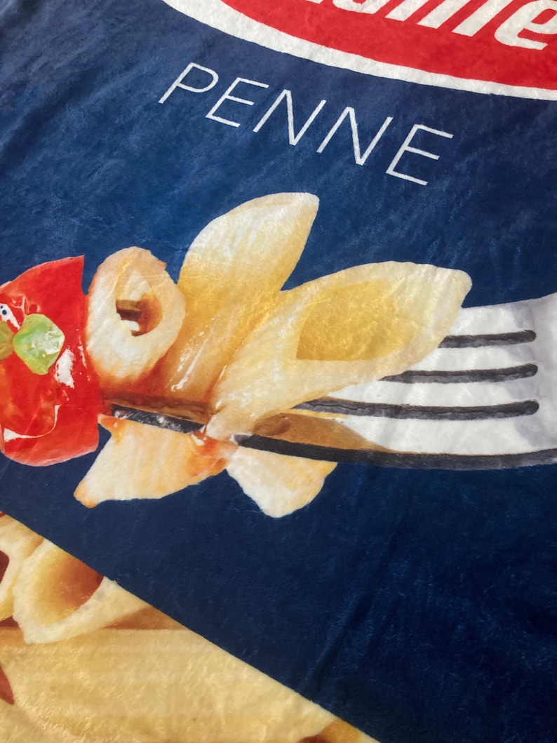 May include: A blue and white box with the word "PENNE" printed on it. The box features a close-up image of cooked penne pasta with a red tomato and a fork.