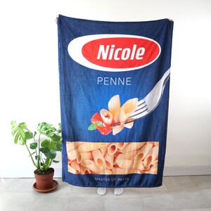 May include: A blue fleece blanket with a printed image of a pasta brand called "Nicole Penne, Master of Pasta". The image features a fork with penne pasta and tomato sauce.