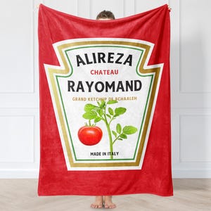 以下が含まれることがあります： 「Alireza Chateau Rayomand Grand Ketchup de Bchaaleh Made in Italy」というテキストが書かれたケチャップボトルのデザインが施された赤いフリースブランケット。