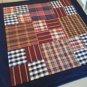 May include: A patchwork quilt with a navy blue border. The quilt is made of various plaid fabrics in shades of red, blue, and white.