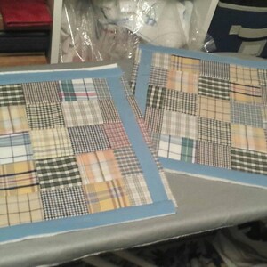 Puede incluir: Dos cojines rectangulares de patchwork con un borde azul. Los cojines est&aacute;n hechos de diferentes telas a cuadros en tonos de marr&oacute;n, beige y azul.