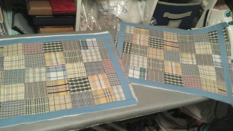 Puede incluir: Dos cojines rectangulares de patchwork con un borde azul. Los cojines est&aacute;n hechos de diferentes telas a cuadros en tonos de marr&oacute;n, beige y azul.
