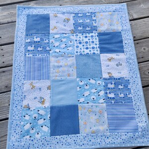 May include: A blue baby quilt with a patchwork design. The quilt is made of various blue fabrics with different patterns, including stars, stripes, and sheep. The quilt is bordered with a light blue fabric with white polka dots.