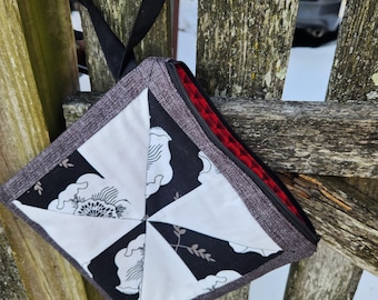 Bolsa con cremallera en negro, blanco y gris con forro rojo. Bloques acolchados con forma de rueda de molino y correa para la muñeca.