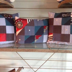 May include: Three decorative pillows made from repurposed fabric. The pillows are blue, red, white, and black with a patchwork design. The pillows are on a metal shelf with a glass top.