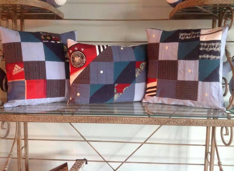 Puede incluir: Tres almohadas decorativas hechas de tela reutilizada. Las almohadas son azules, rojas, blancas y negras con un dise&ntilde;o de patchwork. Las almohadas est&aacute;n en un estante de metal con una tapa de vidrio.