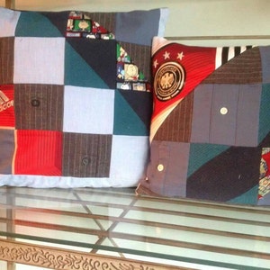Puede incluir: Dos almohadas decorativas hechas de tela reutilizada. La almohada de la izquierda es un mosaico de tela azul, roja y gris con la palabra "adidas" impresa en ella. La almohada de la derecha es un mosaico de tela azul, roja y gris con un bal&oacute;n de f&uacute;tbol y estrellas impresas en ella.