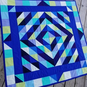 May include: A blue, green, white, and purple quilt with a geometric pattern. The quilt is made of squares and triangles and is arranged in a spiral pattern.