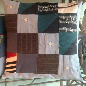 Puede incluir: Una almohada de patchwork con una variedad de telas azules, verdes, marrones y blancas. La almohada est&aacute; hecha de materiales reutilizados, como camisas viejas y recortes de tela.
