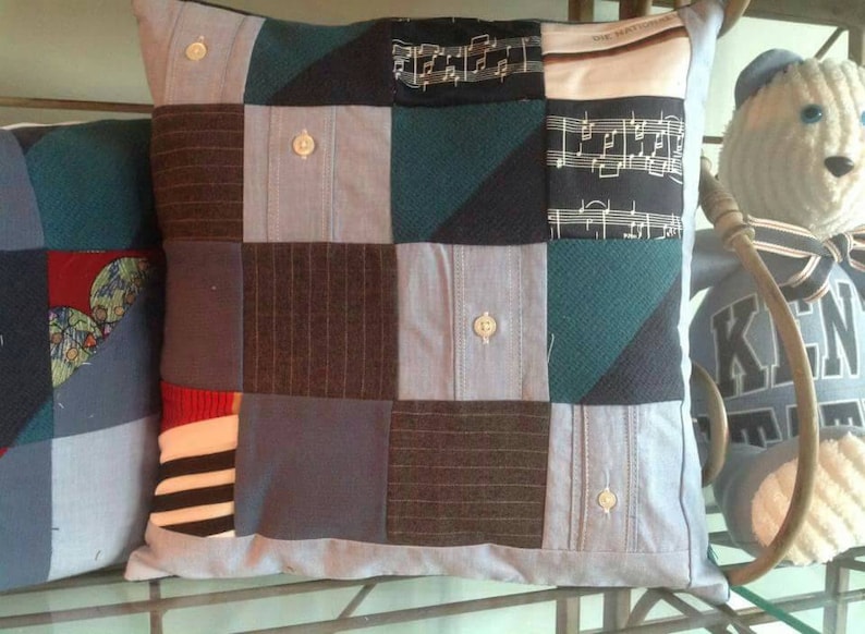 Puede incluir: Una almohada de patchwork con una variedad de telas azules, verdes, marrones y blancas. La almohada est&aacute; hecha de materiales reutilizados, como camisas viejas y recortes de tela.