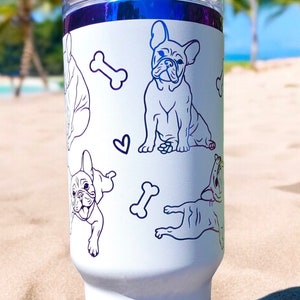 May include: White insulated tumbler featuring blue line art of French Bulldogs, bones, and hearts. The tumbler has a clear lid and a blue metallic rim. The design is repeated around the tumbler.