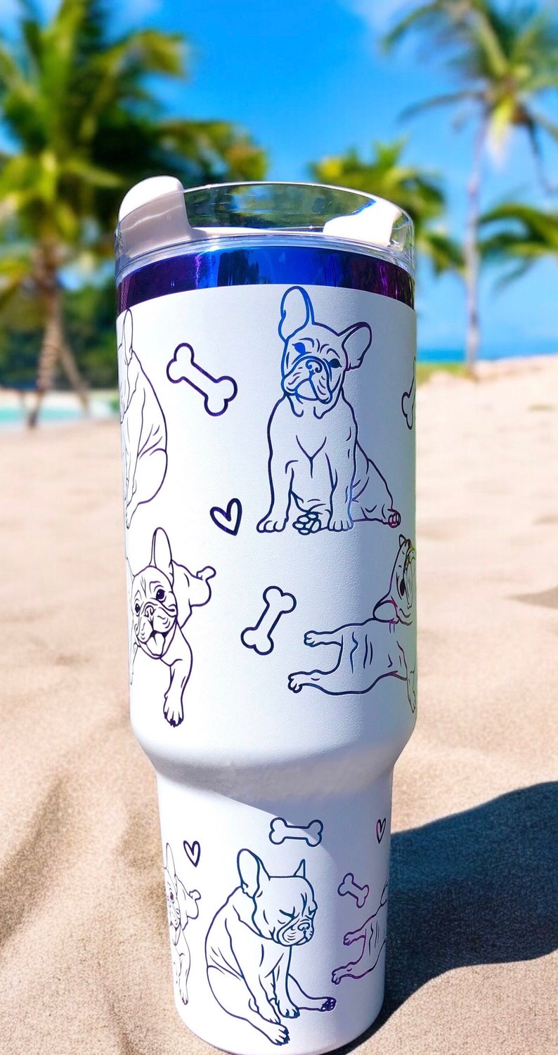 May include: White insulated tumbler featuring blue line art of French Bulldogs, bones, and hearts. The tumbler has a clear lid and a blue metallic rim. The design is repeated around the tumbler.