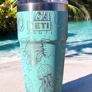 May include: A turquoise YETI tumbler with a silver lid and a silver design of jellyfish on the side.