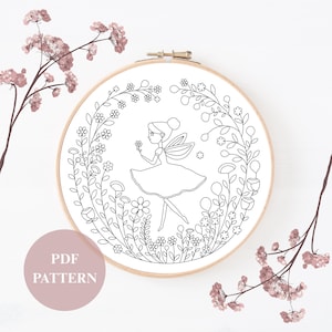 Puede incluir: Un bastidor de bordado en blanco y negro con un hada sosteniendo una flor, rodeada de elementos florales. El texto "PDF PATTERN" está en un círculo rosa. El bastidor de bordado está sobre un fondo blanco.