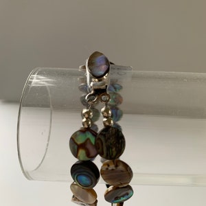 May include: A silver bracelet with a silver clasp and multiple round abalone shell beads. The beads are iridescent with shades of green, blue, brown, and gold.