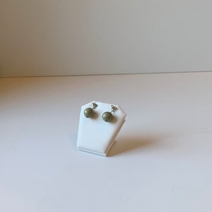 May include: A pair of green stone earrings with silver posts, displayed on a white stand.