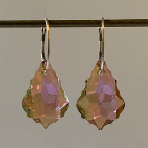 May include: A pair of silver hoop earrings with teardrop-shaped crystal pendants. The crystals are iridescent and have a pink and green hue.