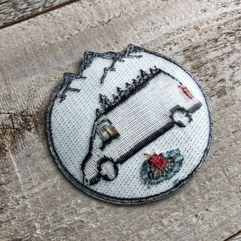 May include: White embroidered patch with a black and white illustration of a van driving into a mountain. The van has a red stripe on the side. The mountain is outlined in black and has a red and white design at the bottom.