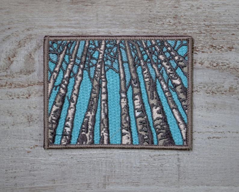 Peut inclure: Patch brod&eacute; repr&eacute;sentant un motif stylis&eacute; d'une for&ecirc;t de bouleaux &agrave; &eacute;corce blanche sur fond de ciel bleu.