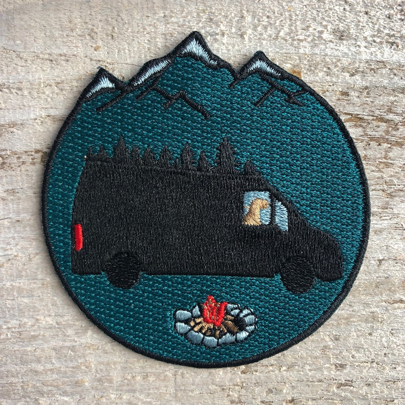 May include: Embroidered patch featuring a black van with a campfire in front of it. The van is silhouetted against a teal blue background with white mountains in the distance.