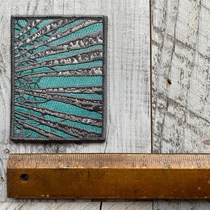 Peut inclure: Un patch carr&eacute; en tissu avec un motif de branches grises sur un fond turquoise.