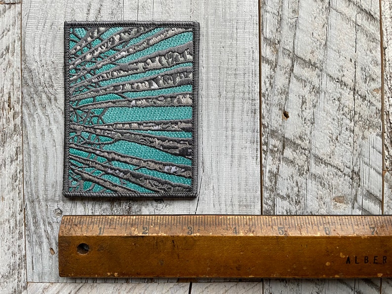 Peut inclure: Un patch carr&eacute; en tissu avec un motif de branches grises sur un fond turquoise.