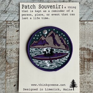 Op de afbeelding: Ronde souvenirpatch met een berg- en meerontwerp in paars, grijs en groen. De patch heeft een witte rand en bevat de tekst "Patch Souvenir" en "Designed in Limerick, Maine."