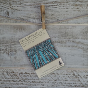 Peut inclure: Une carte blanche avec du texte bleu et noir qui dit "Patch Souvenir: a thing that is kept as a reminder of a person, place, or event that can last a life time." La carte a une illustration bleue et blanche d'arbres en arri&egrave;re-plan. Le bas de la carte indique "www.thinkgreene.net Designed in Limerick, Maine."
