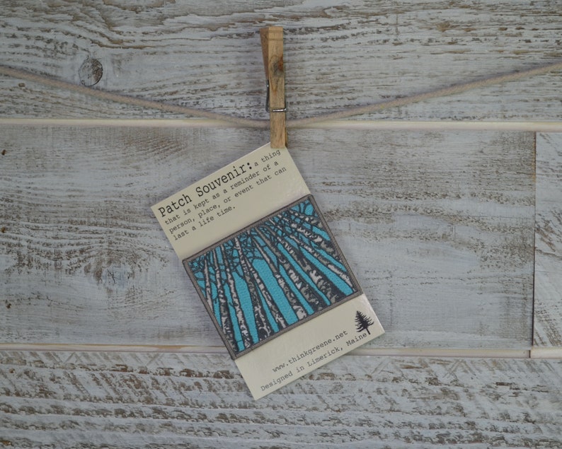 Peut inclure: Une carte blanche avec du texte bleu et noir qui dit "Patch Souvenir: a thing that is kept as a reminder of a person, place, or event that can last a life time." La carte a une illustration bleue et blanche d'arbres en arri&egrave;re-plan. Le bas de la carte indique "www.thinkgreene.net Designed in Limerick, Maine."