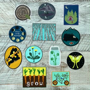 May include: A set of ten colorful stickers featuring various designs, including a forest scene, a moon with stars, a tree stump, a jar with ferns, a dandelion, a camper van, a moth, a bicycle, a row of carrots, and a forest of trees.