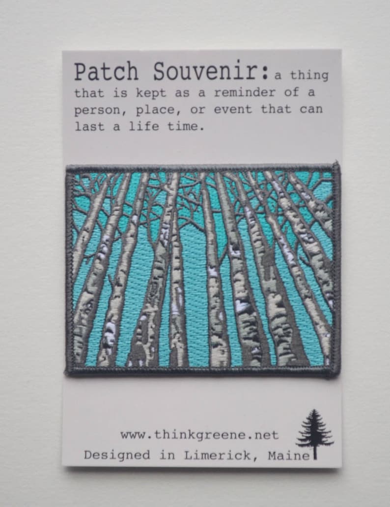 Peut inclure: Un patch brod&eacute; turquoise et gris repr&eacute;sentant une for&ecirc;t de bouleaux. Le texte "Patch Souvenir: a thing that is kept as a reminder of a person, place, or event that can last a life time." est imprim&eacute; sous le patch. Le texte "www.thinkgreene.net Designed in Limerick, Maine" est imprim&eacute; sous le texte.