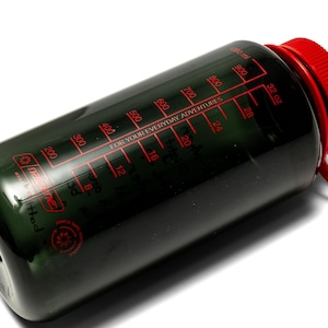 May include: A dark green water bottle with a red cap and measurements in ounces and milliliters. The bottle has a red scale with measurements up to 32 oz and 1000 ml. The text "FOR YOUR EVERYDAY ADVENTURES" is printed on the bottle.